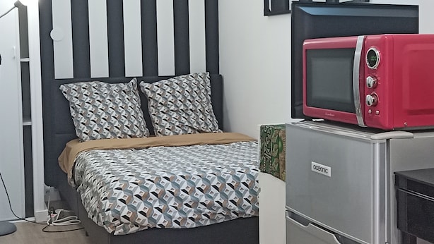 A bedroom with a bed, a red microwave, and a small desk with a computer. - Cosy Vallée Studio (Pau)