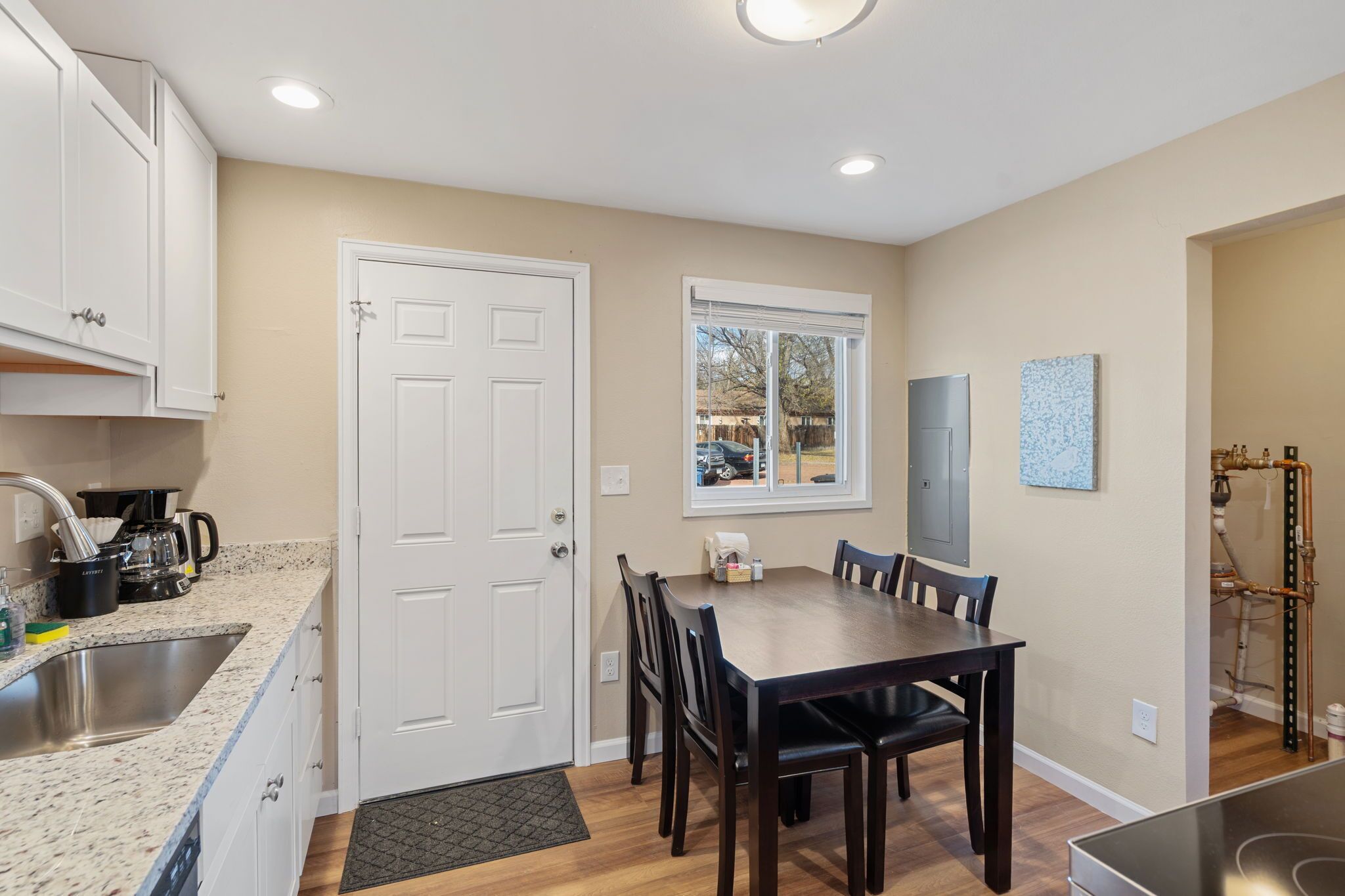 A kitchen with a sink, cabinets, a window, and a dining table with chairs.
