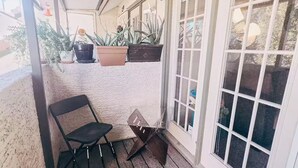 A covered porch with a wooden floor, a black chair, and potted plants. - Home Away from Home in Mesa (Mesa)