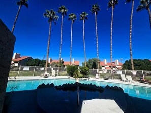 Une piscine, avec un ciel bleu azur et de grands palmiers en arrière-plan.
