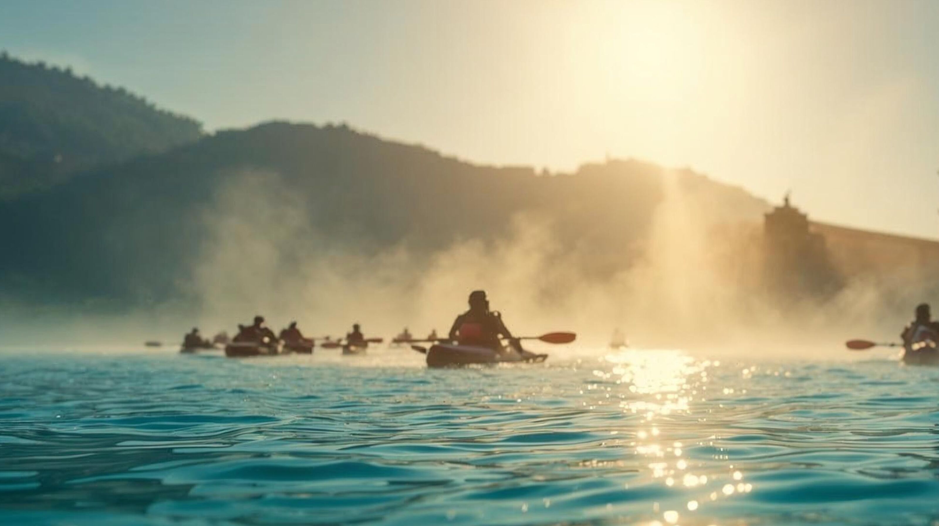 A group of kayakers on a calm body of water with a misty mountain backdrop.
