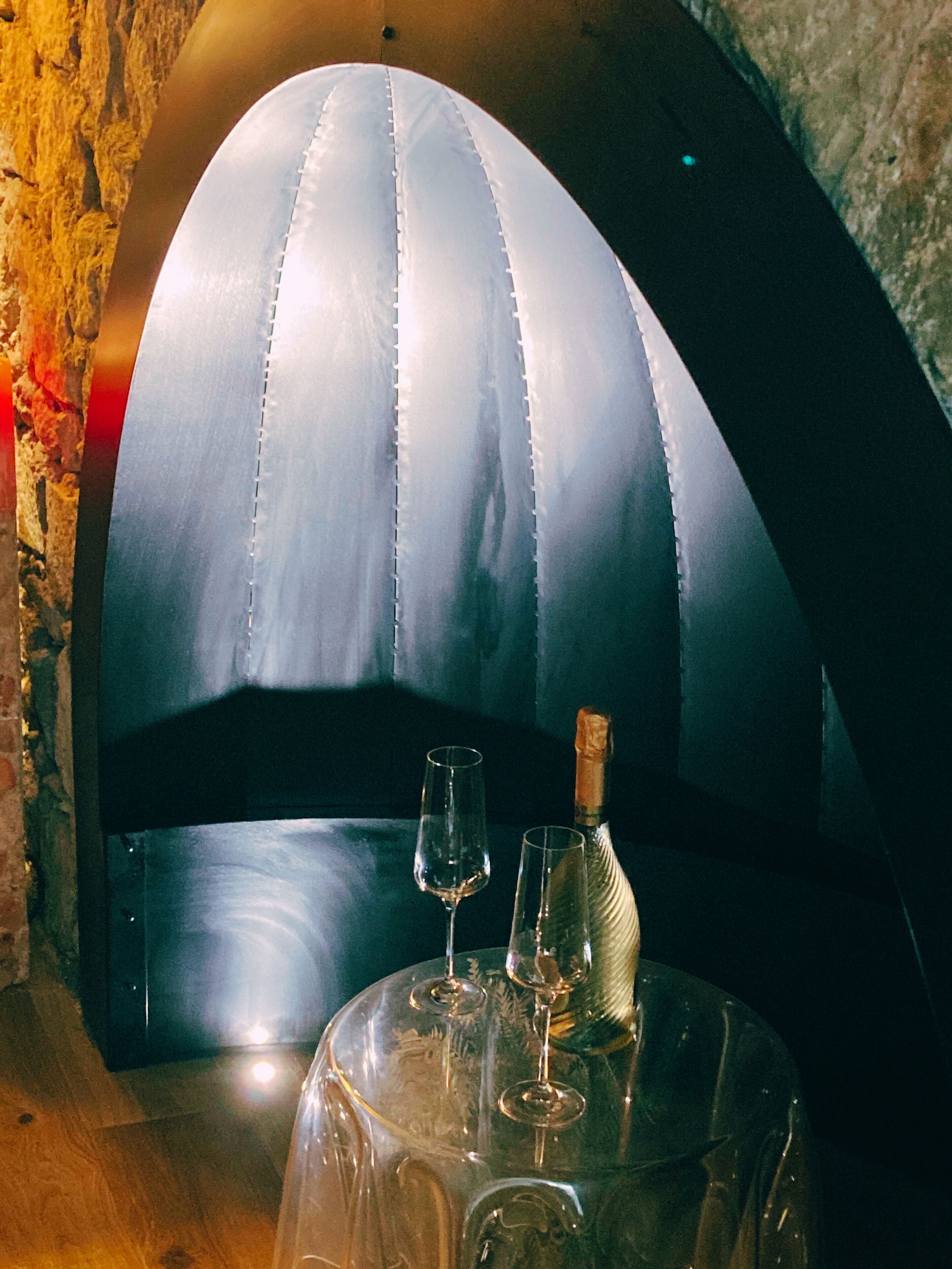 A table with a glass dome-shaped seating area, a bottle of champagne, and two glasses.