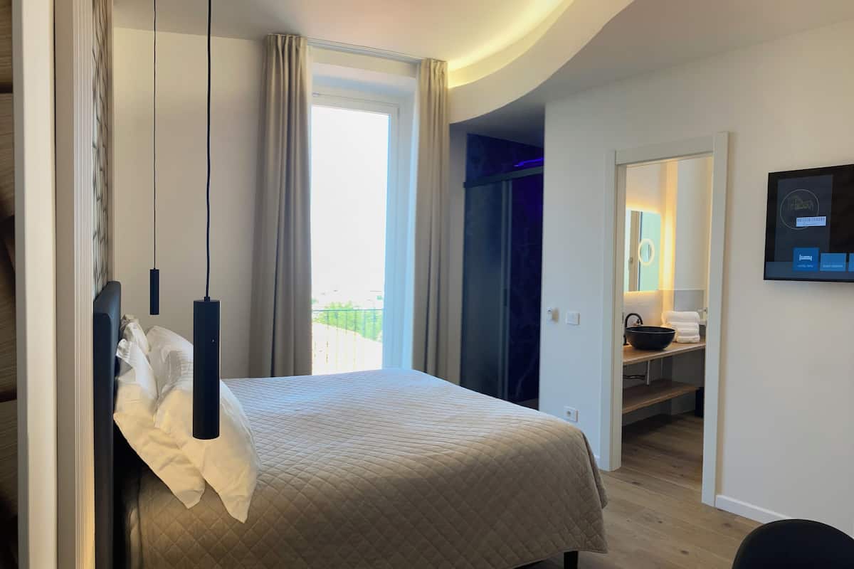 A hotel room with a bed, a desk, a bathroom with a mirror and sink, and a TV on the wall.