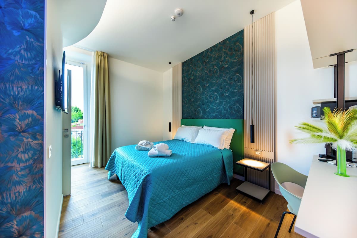 A modern hotel room with a large bed, a bedside table, a chair, and a view of the outdoors.