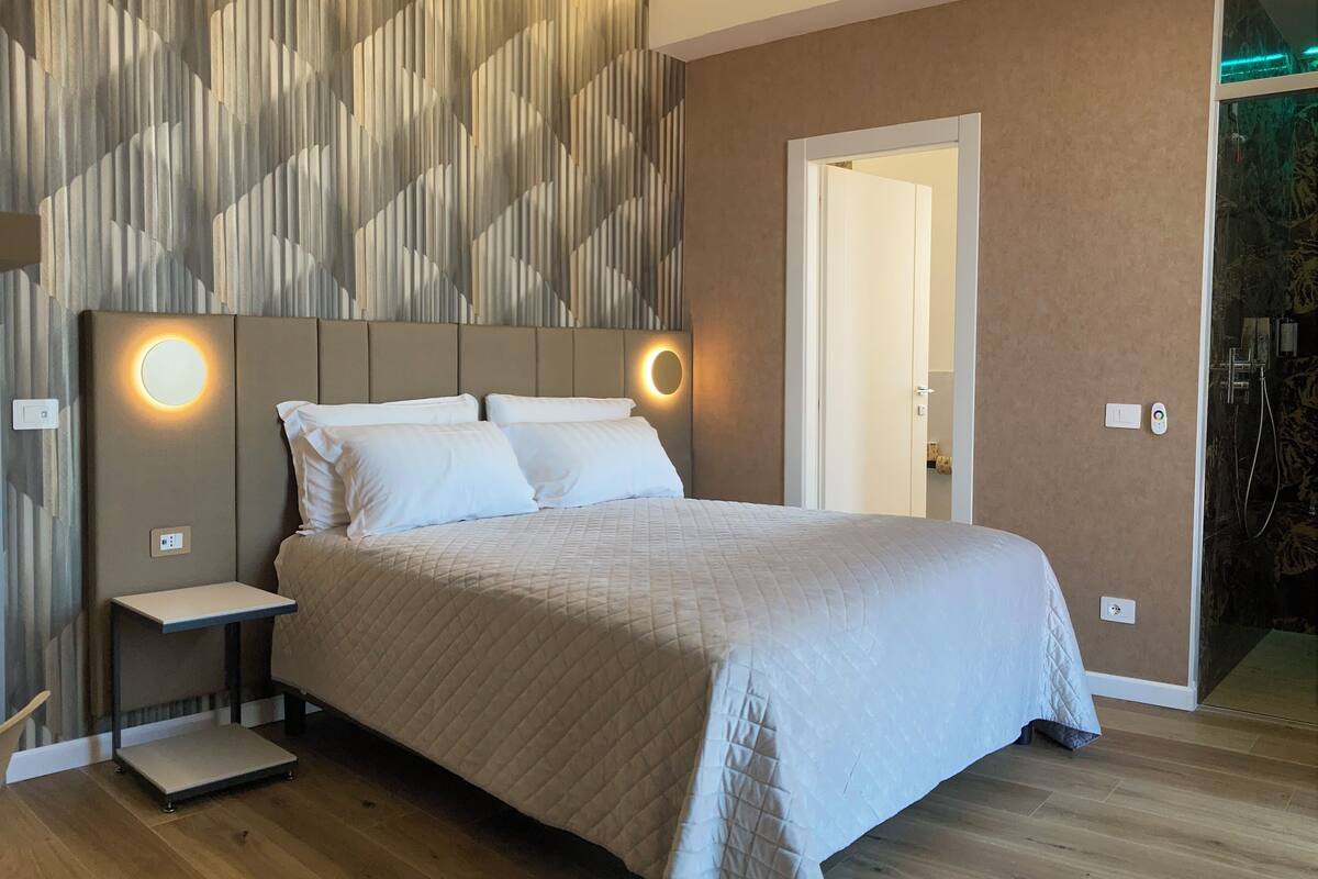A modern bedroom with a large bed, bedside tables, and a wall-mounted light fixture.