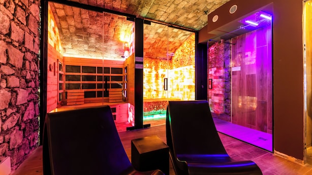 A spa room with two black massage chairs, a stone wall, and a wooden ceiling. - ARICCIA LUXURY HOUSE (Ariccia)