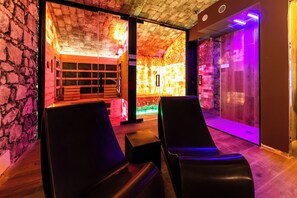 Une salle de spa équipée de deux fauteuils de massage noirs, d’un mur en pierre et d’un plafond en bois.