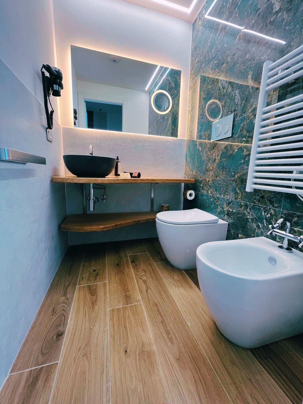 Ein modernes Badezimmer mit einem Holzkosmetikschrank, einem großzügigen Waschbecken und zwei Bidet-Einheiten.