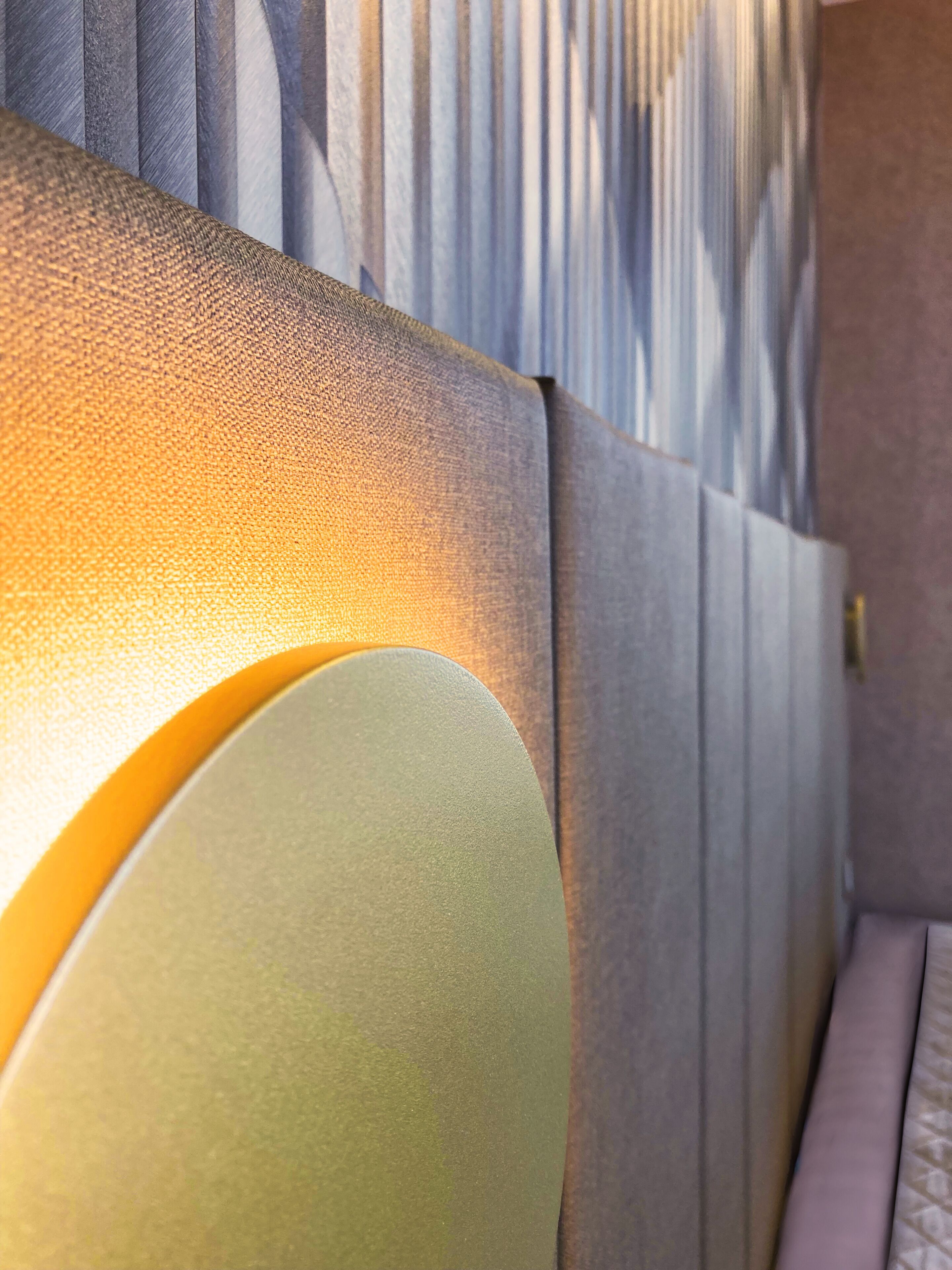 A close-up of a textured wall with vertical lines and a soft, illuminated light fixture.