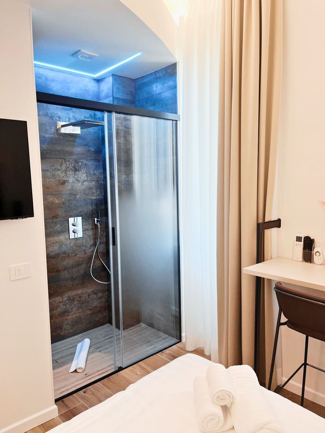 A modern bathroom with a glass shower enclosure, a wooden wall, and a small desk with a chair.