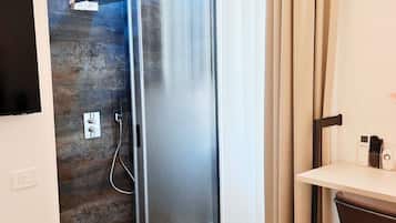 A modern bathroom with a glass shower enclosure, a wooden wall, and a small desk with a chair.
