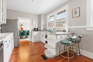 A modern kitchen with white cabinetry, a granite countertop, and a built-in island with bar stools. - Cottontown Bungalow - Fast WiFi - Walk Downtown (Columbia)