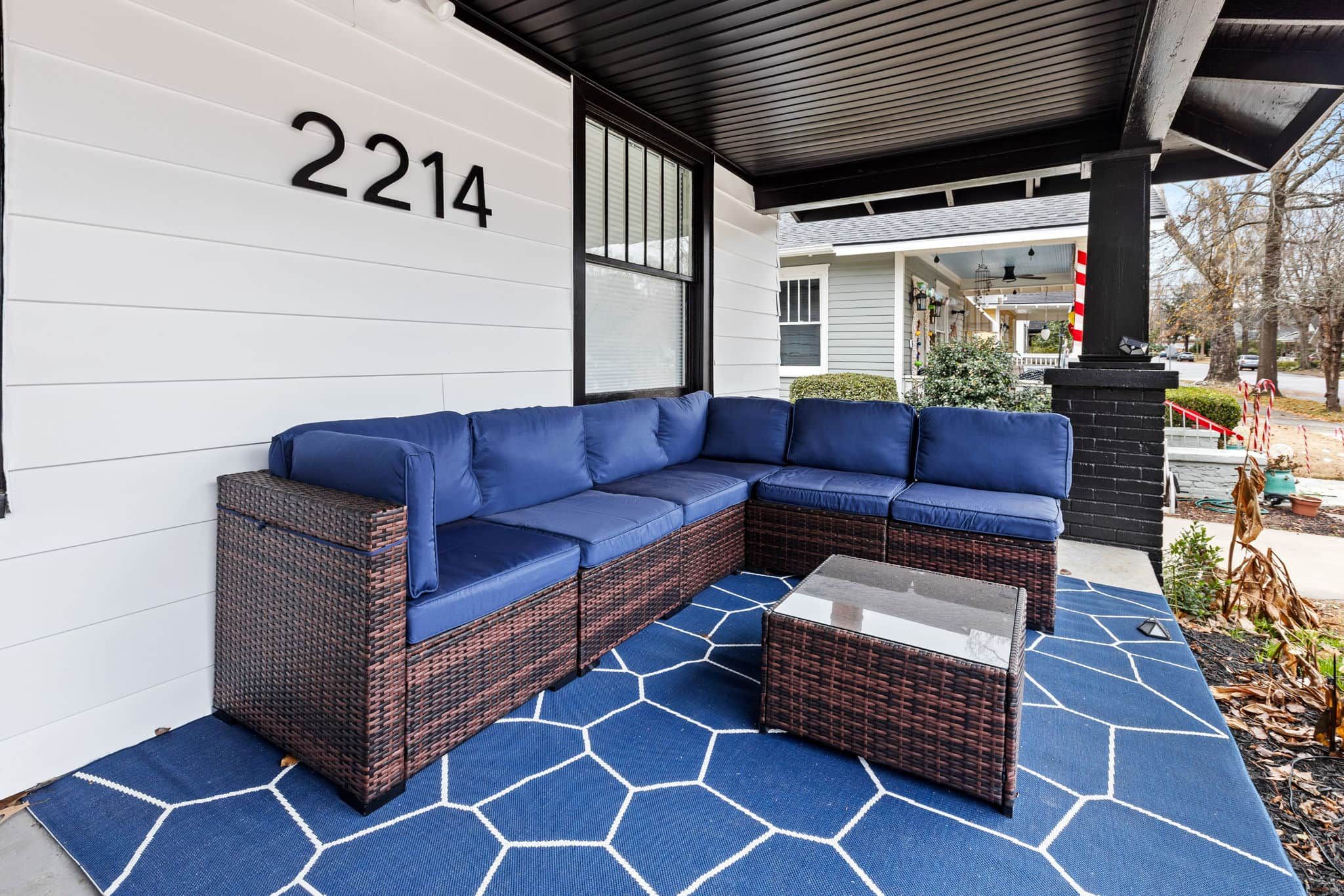 Une véranda avec un canapé d’angle bleu et une petite table, le numéro 2214 est inscrit sur le mur, et un tapis à motifs.