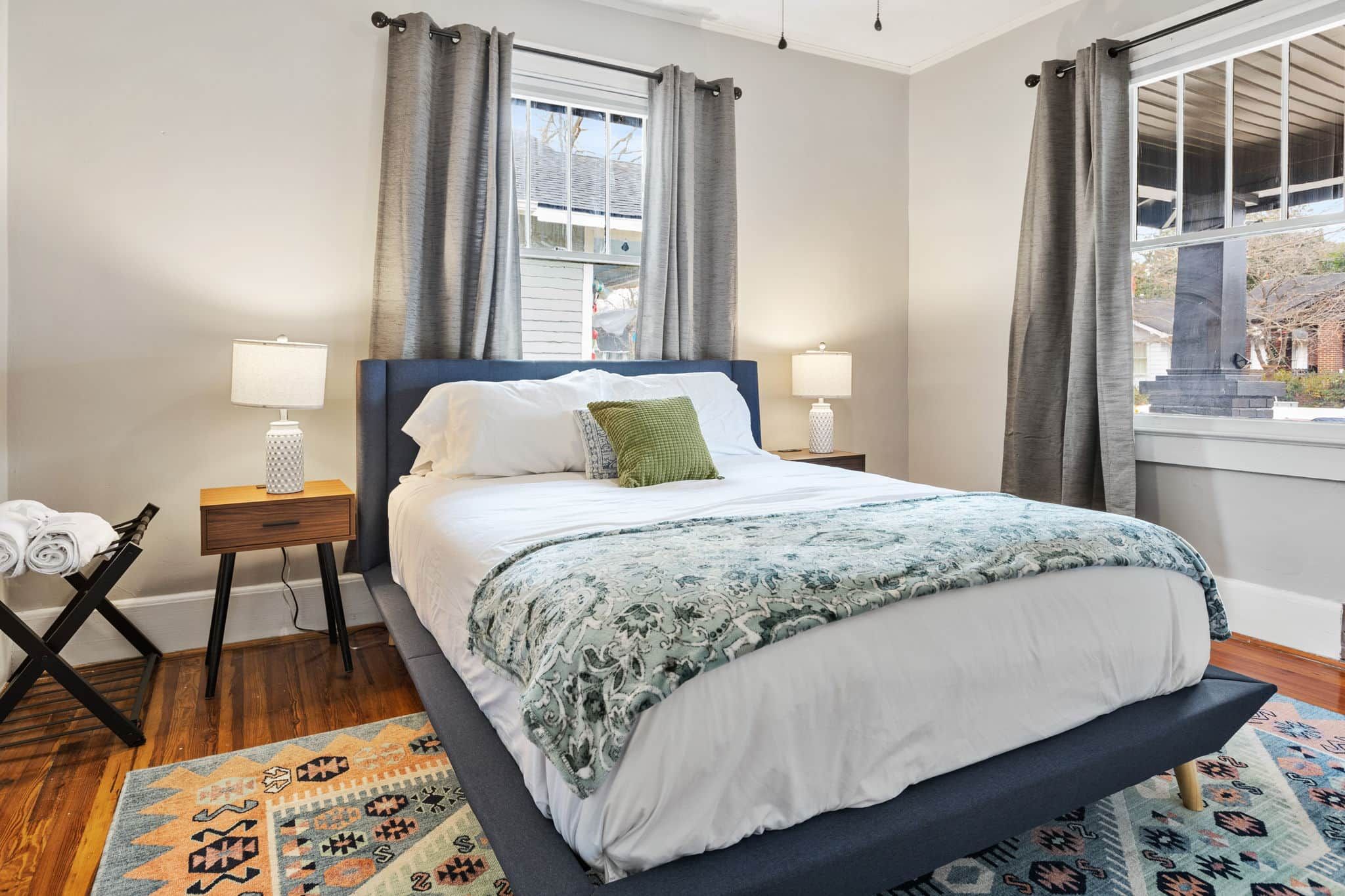 A neatly arranged bedroom with a bed, two bedside tables with lamps, a window with curtains, and a patterned rug.