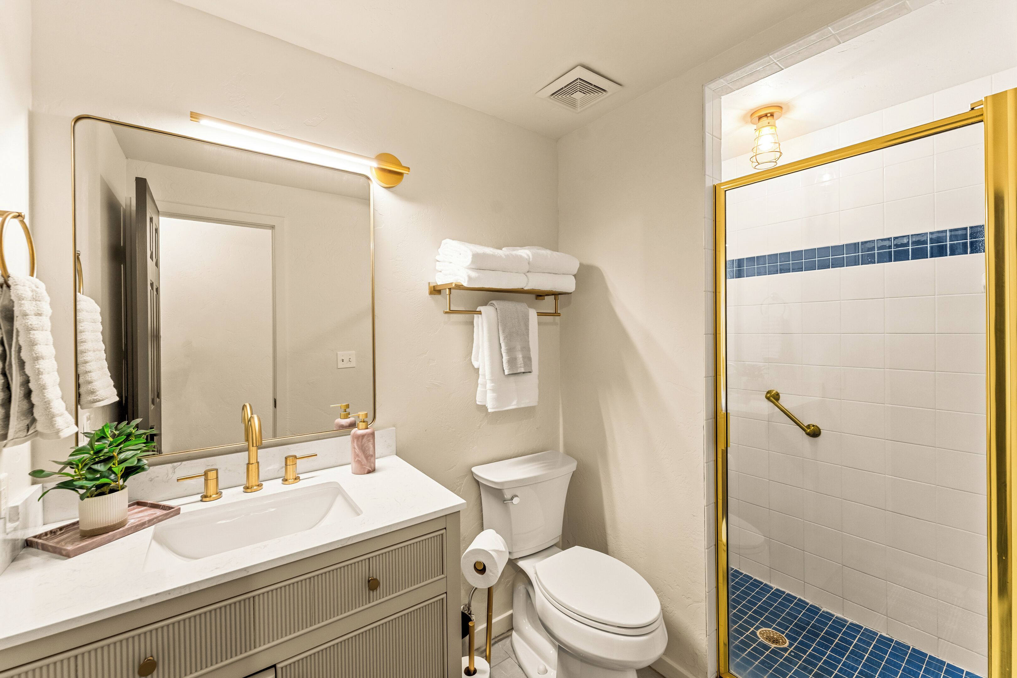 A bathroom with a white sink, gold faucets, a toilet, and a shower with a gold frame.