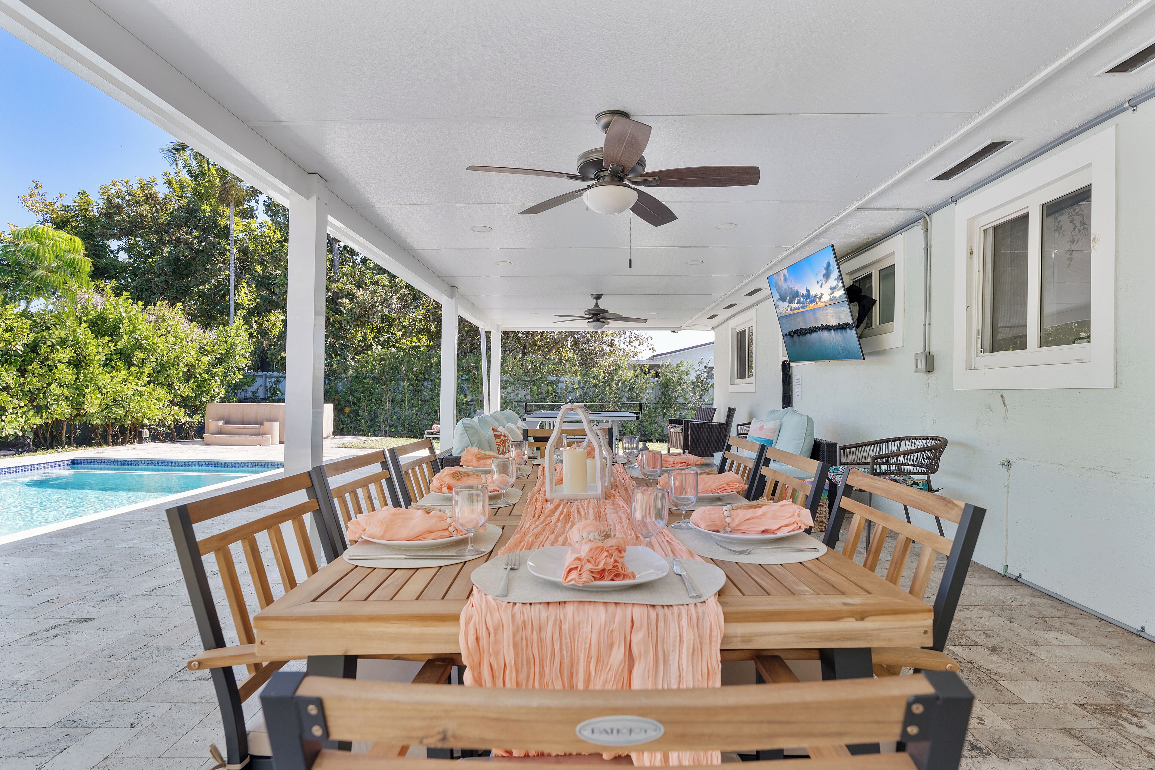 A covered outdoor dining area with a pool, wooden tables, and ceiling fans.