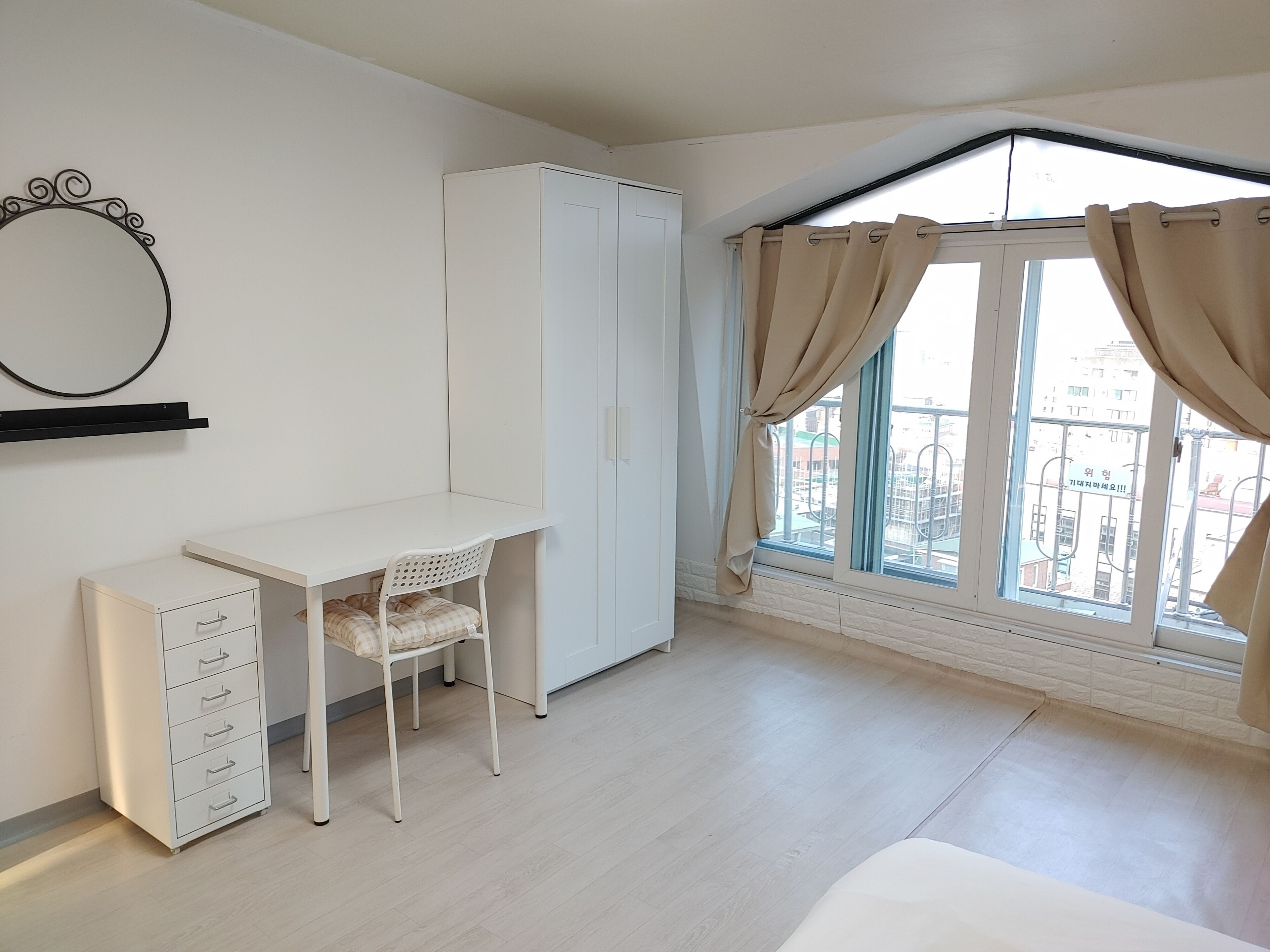 A bedroom with a desk, chair, wardrobe, and a window with curtains.