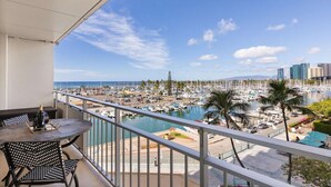A balcony with a table and chairs, overlooking a marina with boats and a city skyline. - 4th Fl Ilikai | Pool | AC | Marina View (Honolulu)