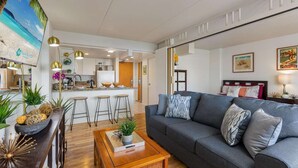 A modern living room with a grey sofa, wooden coffee table, and a kitchen in the background. - 4th Fl Ilikai | Pool | AC | Marina View (Honolulu)