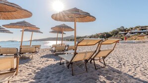 Een strand met ligbedden en rieten parasols, een heldere lucht en een wateroppervlak in de verte.