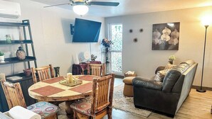 A dining area with a round wooden table and chairs, a black leather sofa, and a TV mounted on the wall.