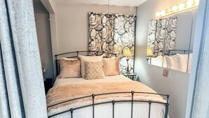 A neatly made bed with a metal frame, a patterned headboard, and a bedside lamp.