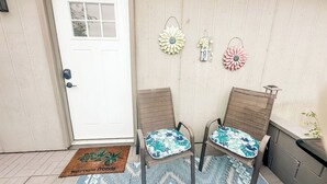 A porch with two wicker chairs, a white door, and decorative wall hangings.