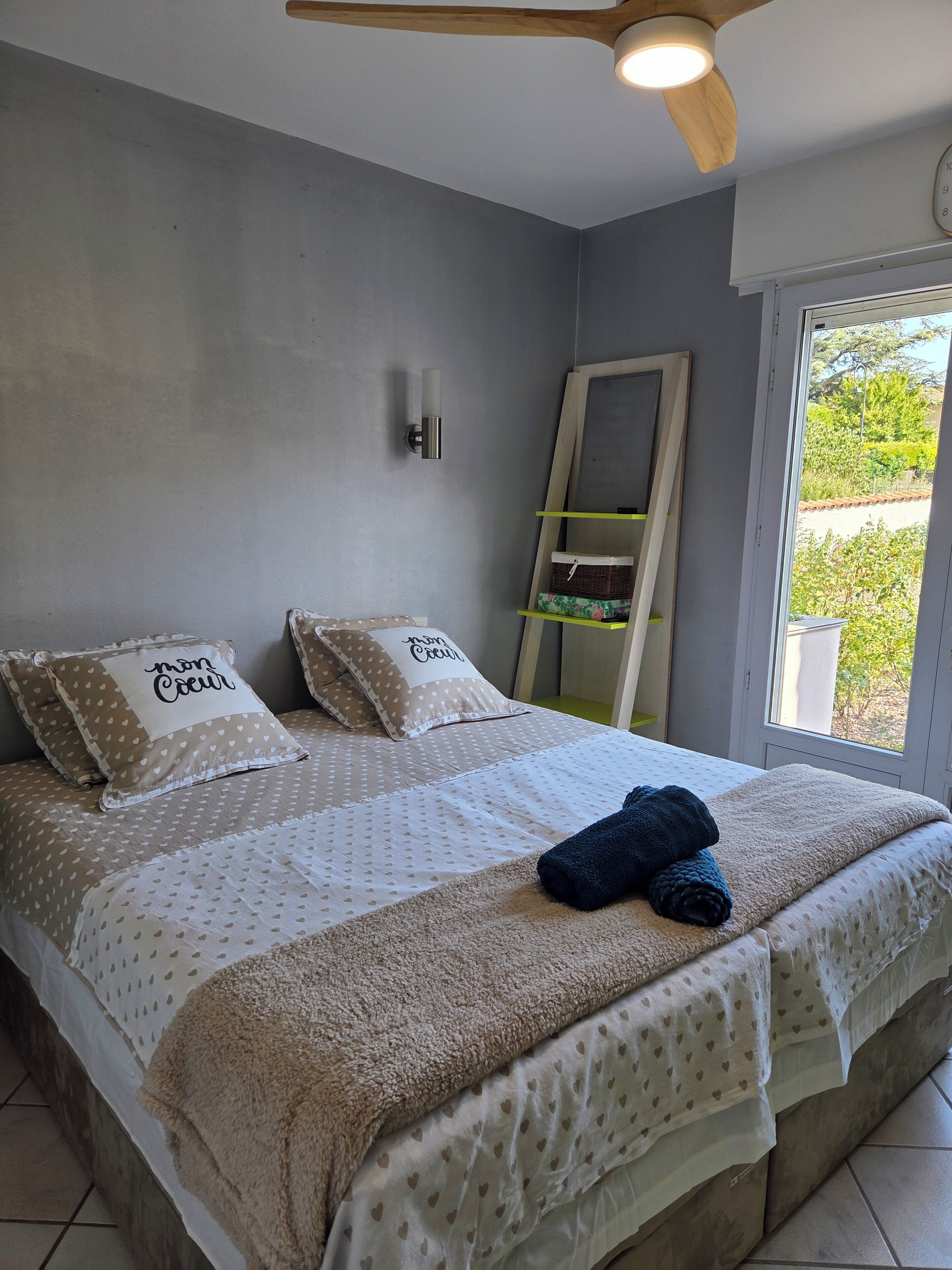 A bedroom with a bed, pillows, a bedside table, a mirror, and a window with a view.