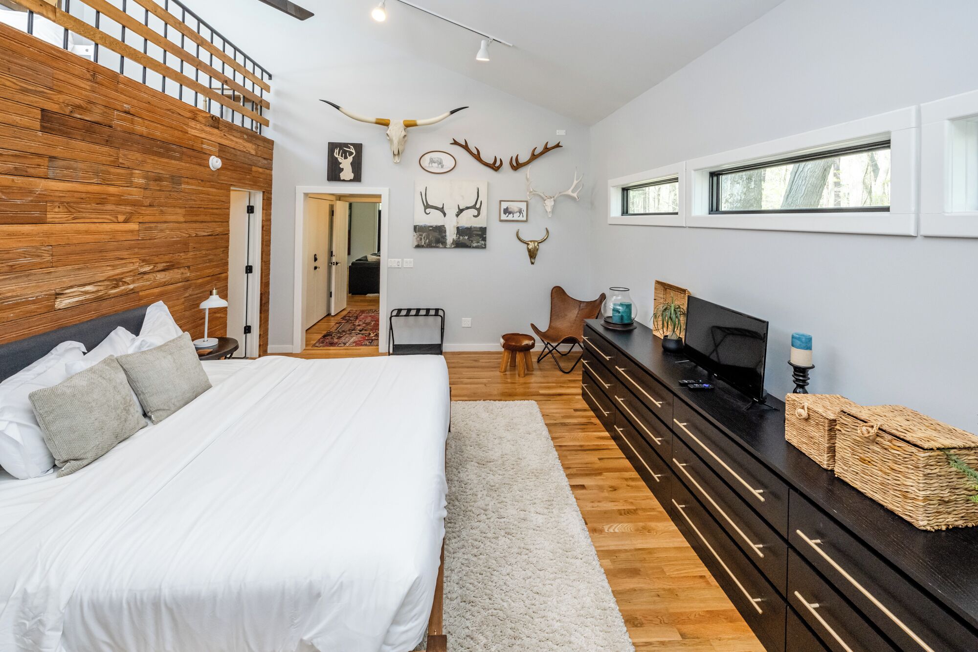 A bedroom with a large bed, wooden headboard, a dresser, a television, and wall-mounted antler decorations.