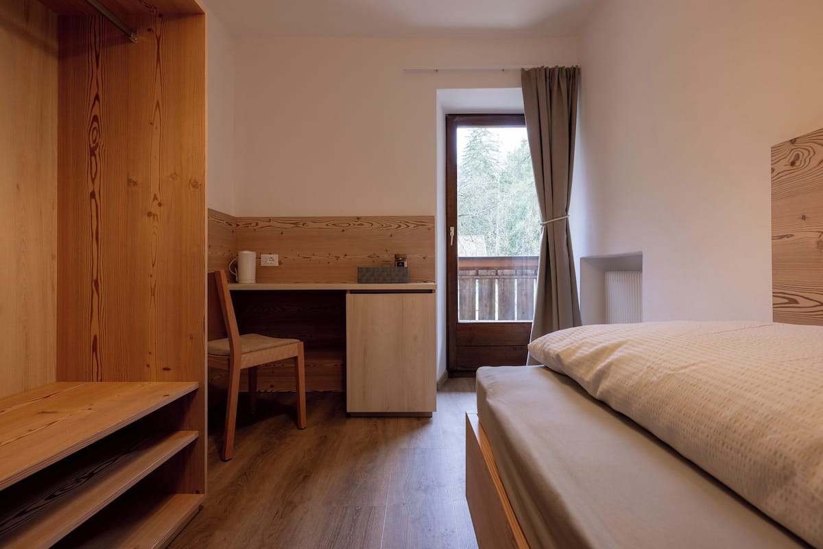 A small, cozy room with a wooden desk, a chair, a bed, and a window with curtains.