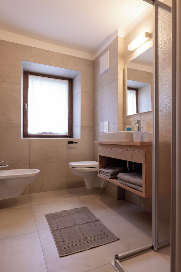 A modern bathroom with a large window, a sink, a toilet, and a mirror. - SAN PIETRO Dolomiti Small Budget Hotel (San Pietro Valle)