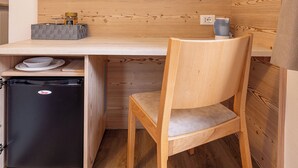 Un angolo cottura compatto con frigorifero integrato, una scrivania in legno, una sedia e una TV a schermo piatto montata a parete.