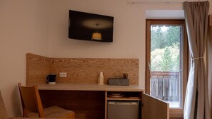 Una camera compatta con una scrivania in legno, un piccolo frigorifero, una sedia e una TV a parete.