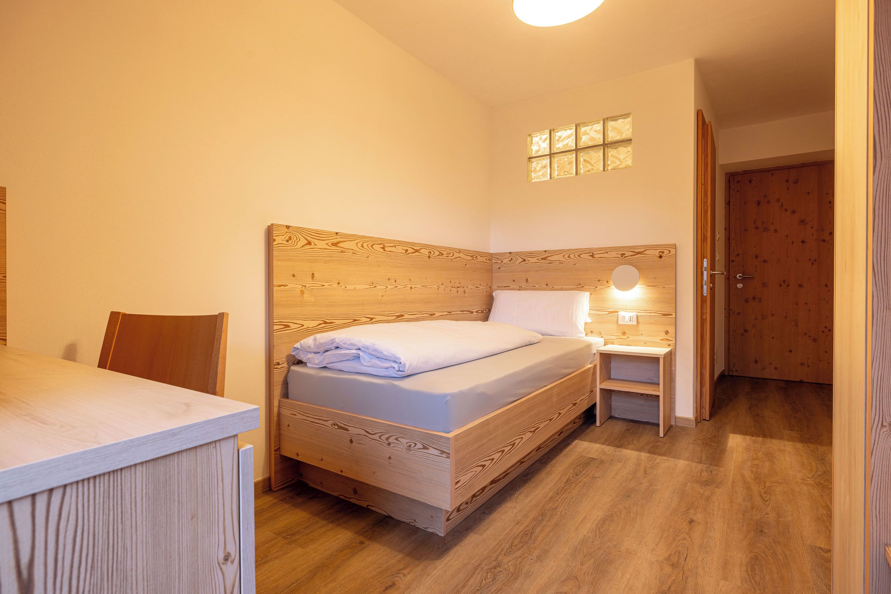A wooden bed with a headboard, a bedside table, and a small window with light.
