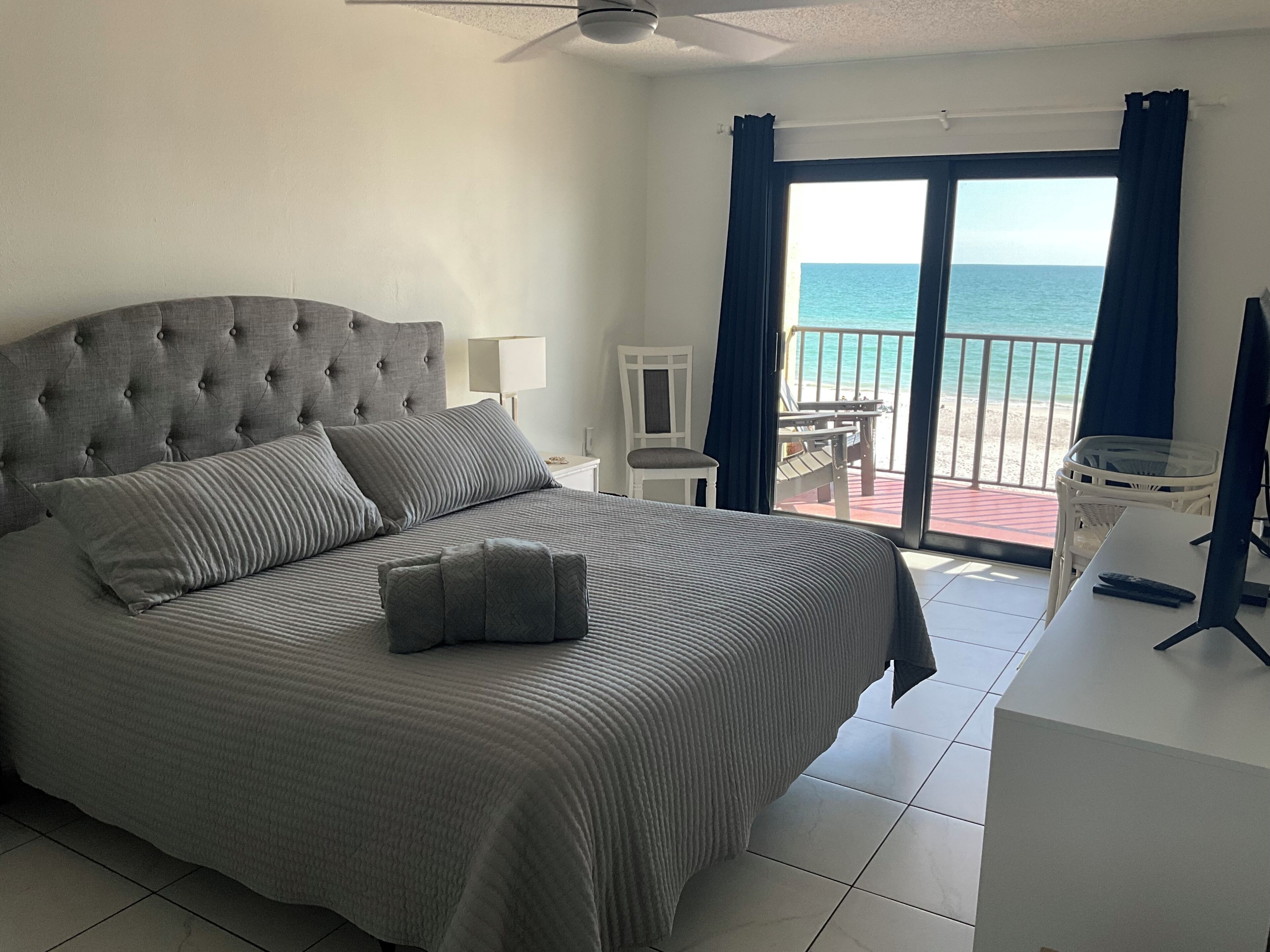 A bedroom with a large bed, a desk, and a view of the sea.