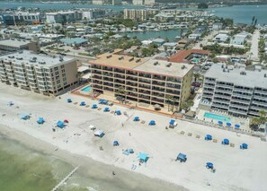 An aerial view of a coastal hotel with multiple floors, a beach area with umbrellas, and a marina in the background. - ON THE BEACH! 3-bedroom condo in fabulous Madeira Beach. Amazing views. (Madeira Beach)