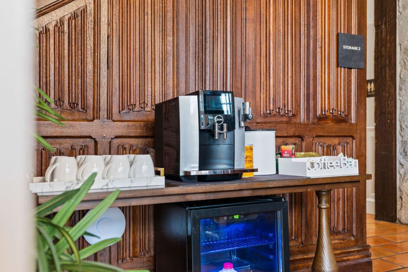 Eine Kaffeestation mit Kaffeemaschine, Tassen und einem Kühlschrank.