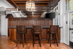 Un coin bar avec des lambris en bois, trois tabourets et un lustre.