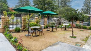 An outdoor patio area with tables and chairs, surrounded by a stone wall and greenery. - First floor Cozy king room w/ Wine Country Charm (Santa Rosa)