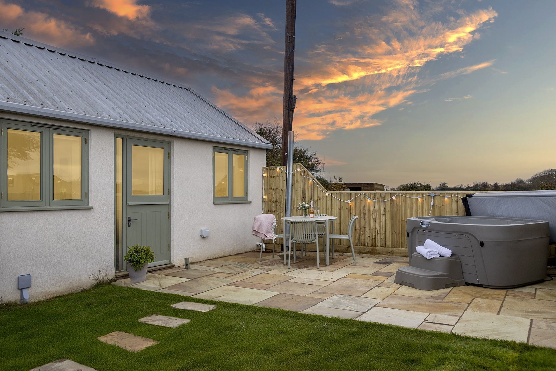 A patio with a hot tub, a table with chairs, and a wooden fence.