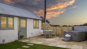 A patio with a hot tub, a table with chairs, and a wooden fence. - The Stables at Sturt Farm Courtyard - Beautiful dog friendly home in the Cotswolds with a hot tub (Burford)