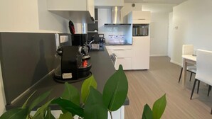 Een moderne keuken met witte kastjes, een koffieapparaat en een eethoek met witte stoelen.