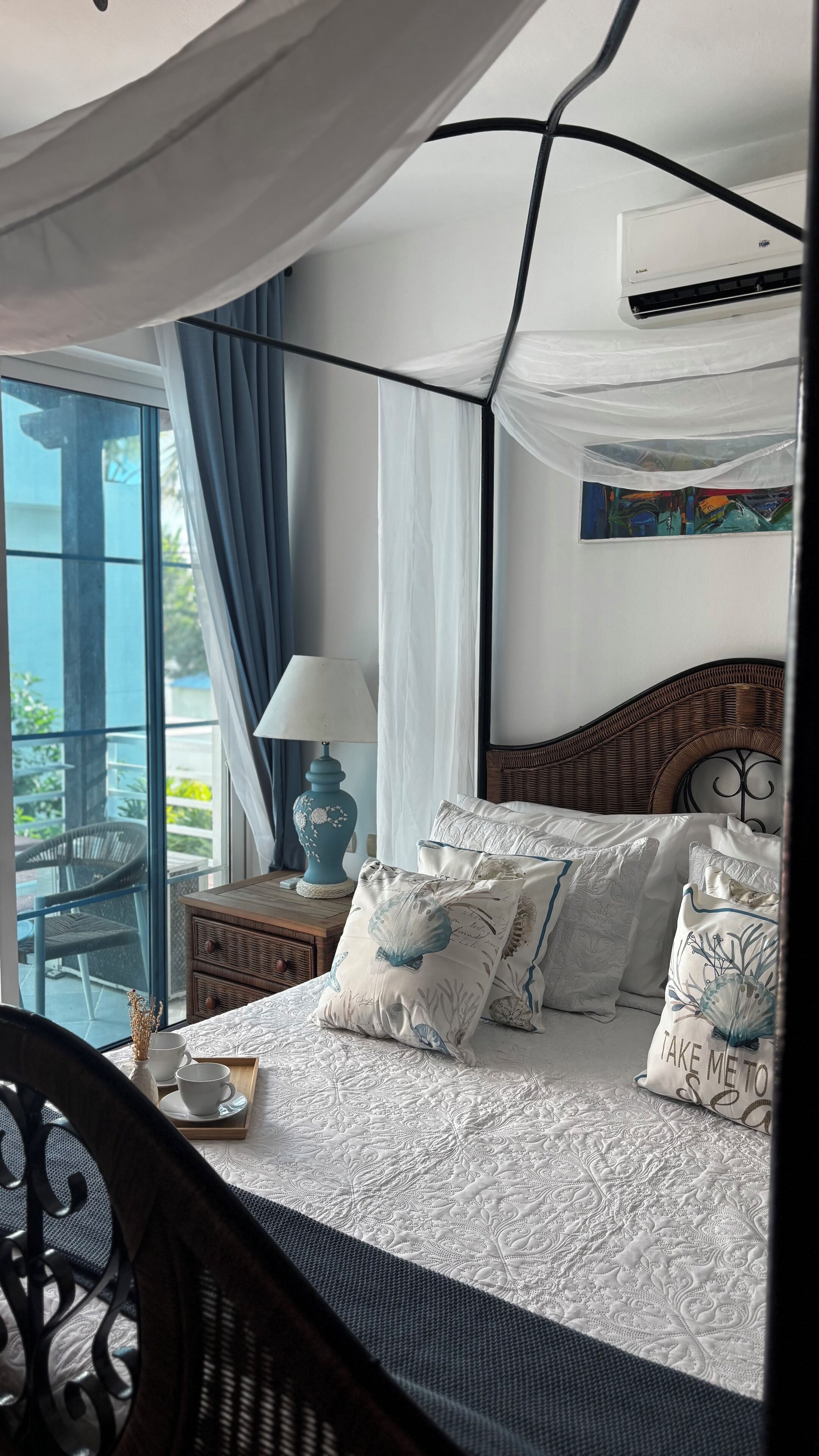 Een slaapkamer met een bed, nachtkastje, lamp en uitzicht op het buiten.