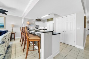 A modern kitchen with white cabinetry, a central island with bar stools, a microwave, and a refrigerator. - ☀️Gulf FRONT-Pools+Hot Tubs-Emerald Beach 2333☀️ (Panama City Beach)