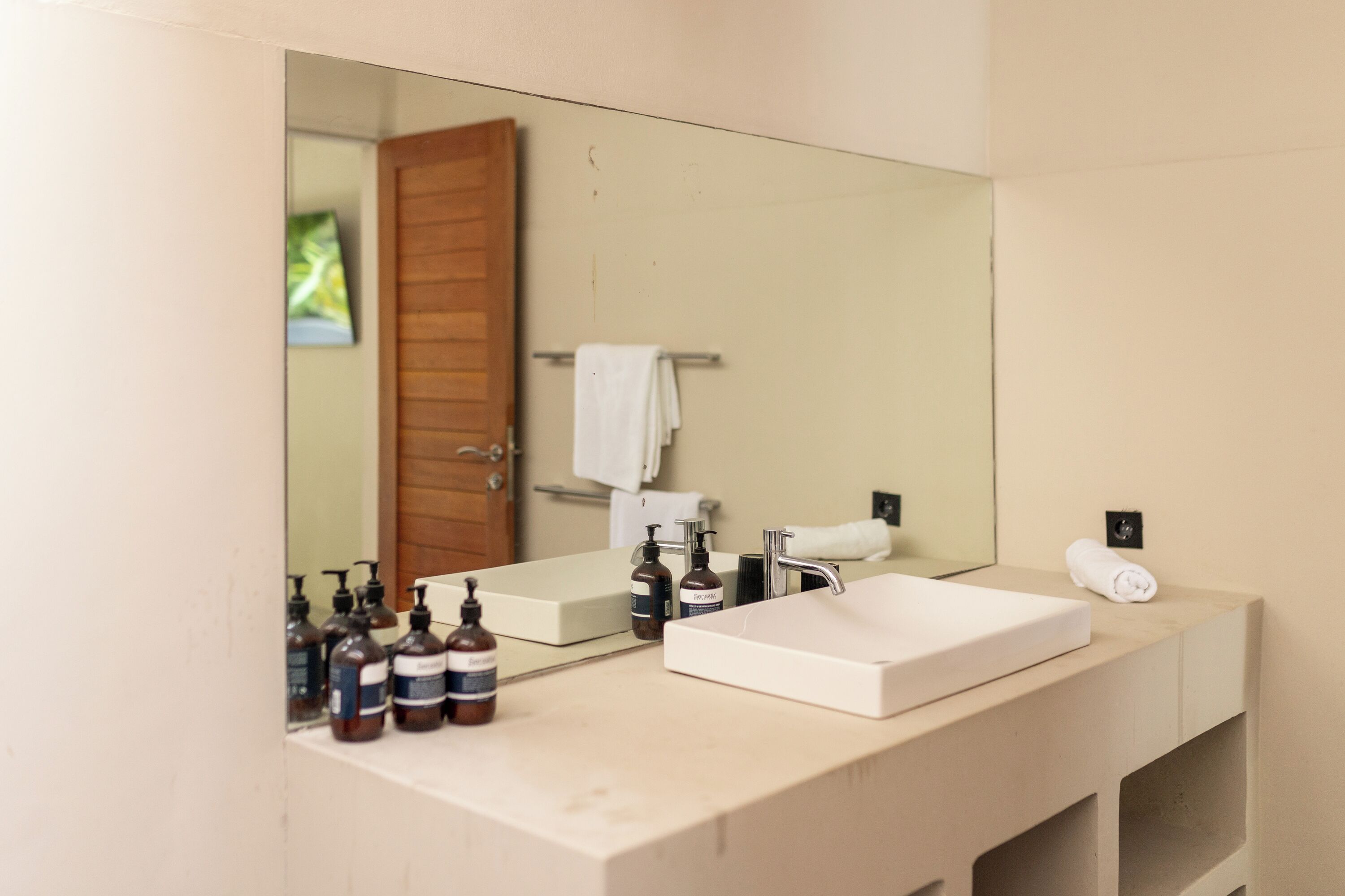 Une salle de bain avec un grand miroir, un lavabo blanc et plusieurs flacons de produits de toilette.