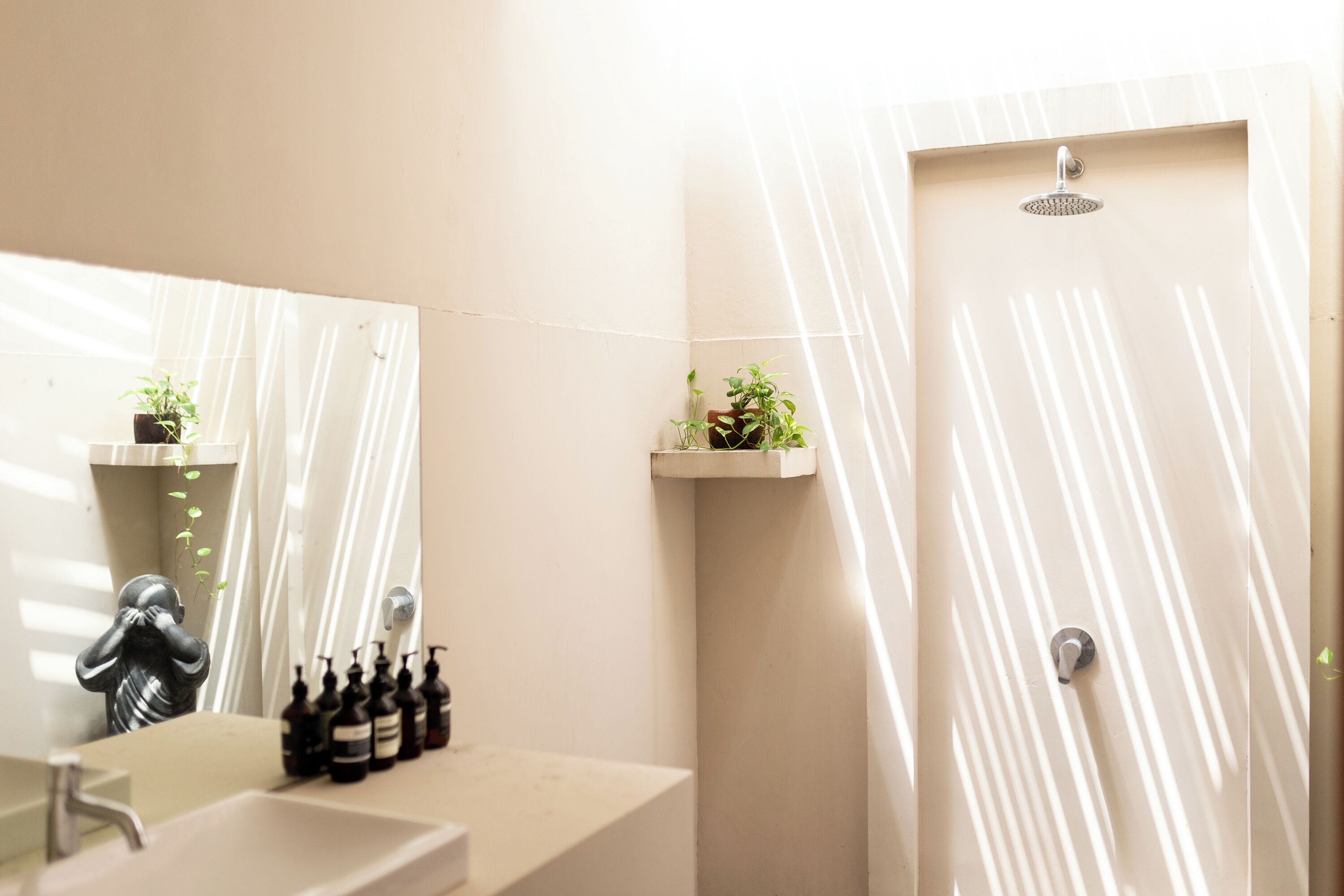 A bathroom with a sink, mirror, shower, and two potted plants.