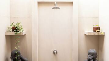 A bathroom with a beige door, a showerhead, and two small shelves with plants.