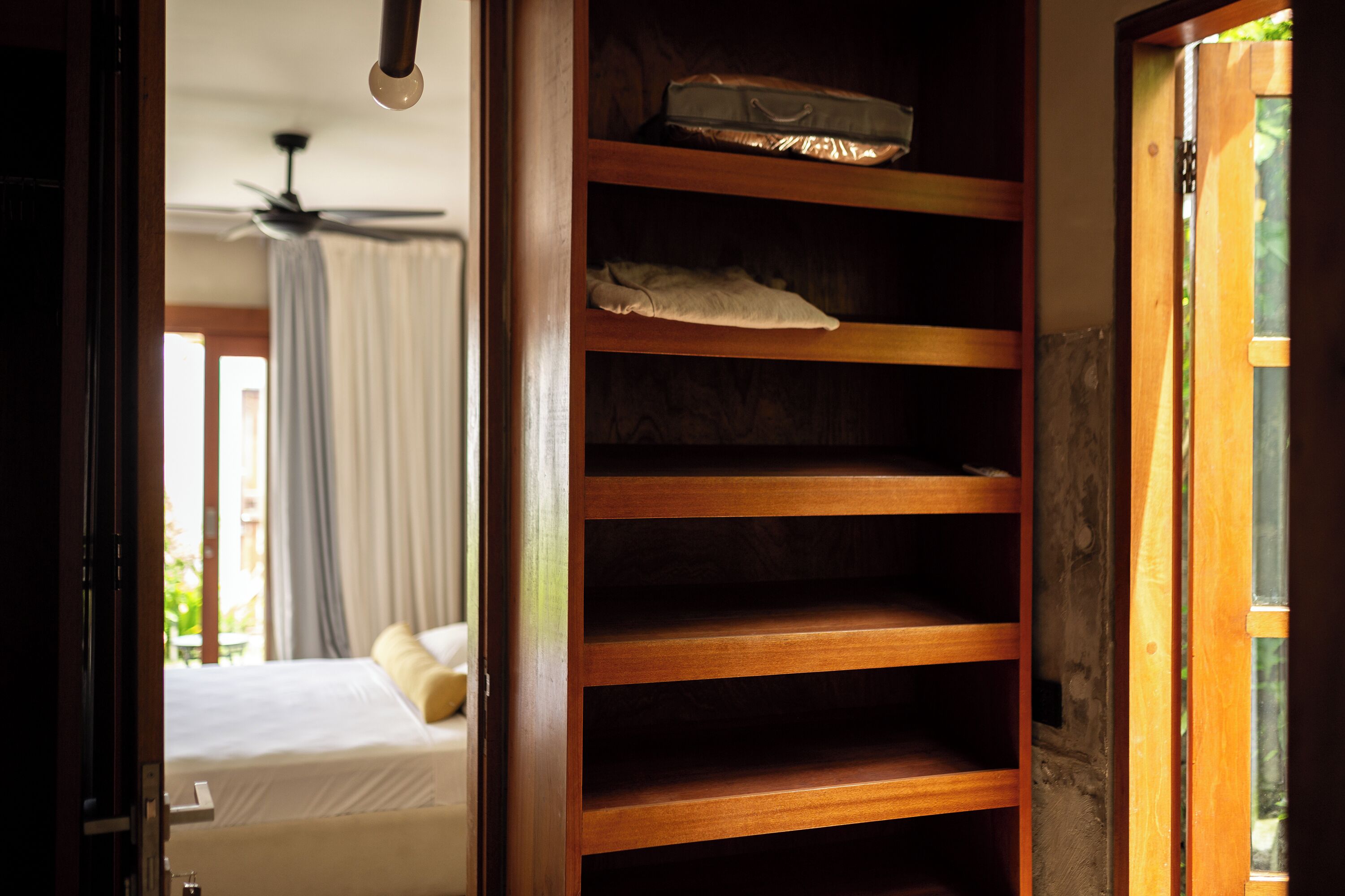 Ein Hotelzimmer mit Holzschrank, einem Bett mit weißer Bettwäsche und einem Deckenventilator.