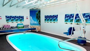 Una piscina interior amb sòl de vidre, envoltada de parets decorades amb murals amb motius de platja.