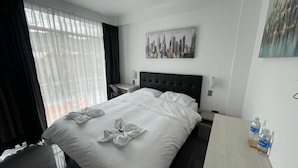 A hotel room with a large bed, a bedside table, a nightstand, and a cityscape painting on the wall. - Hotel Oti (Cajamarca)
